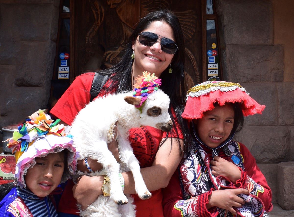 mulher jovem segurando uma alpaca peruna com duas meninas quechuas