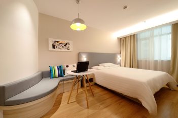 quarto de hotel bem iluminado com cama, luminária, laptop.